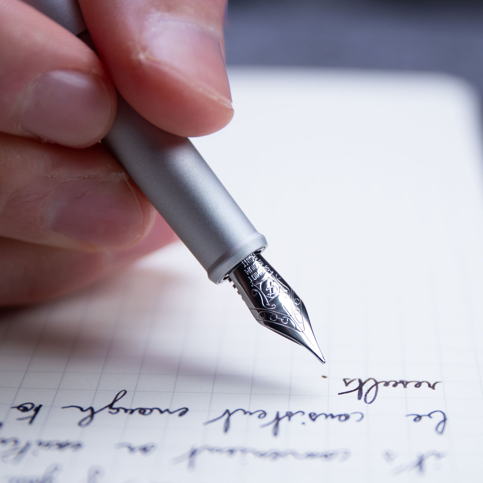 close up of a hand writing with a silver fountain pen on lined paper#45031769735471