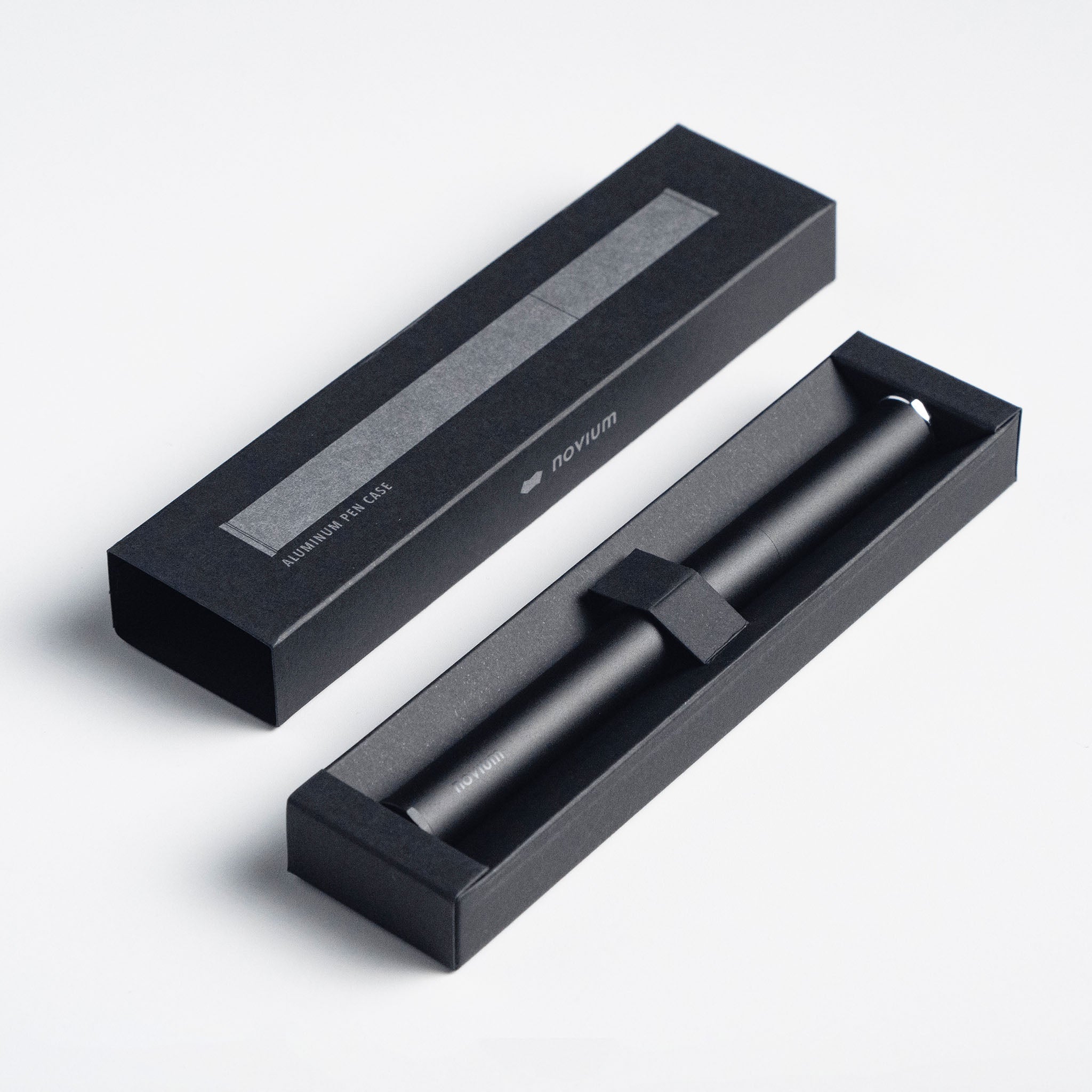 A sleek matte black aluminum pen case is minimalist in design and its packaging box that reads "Aluminum Pen Case" in small silver text