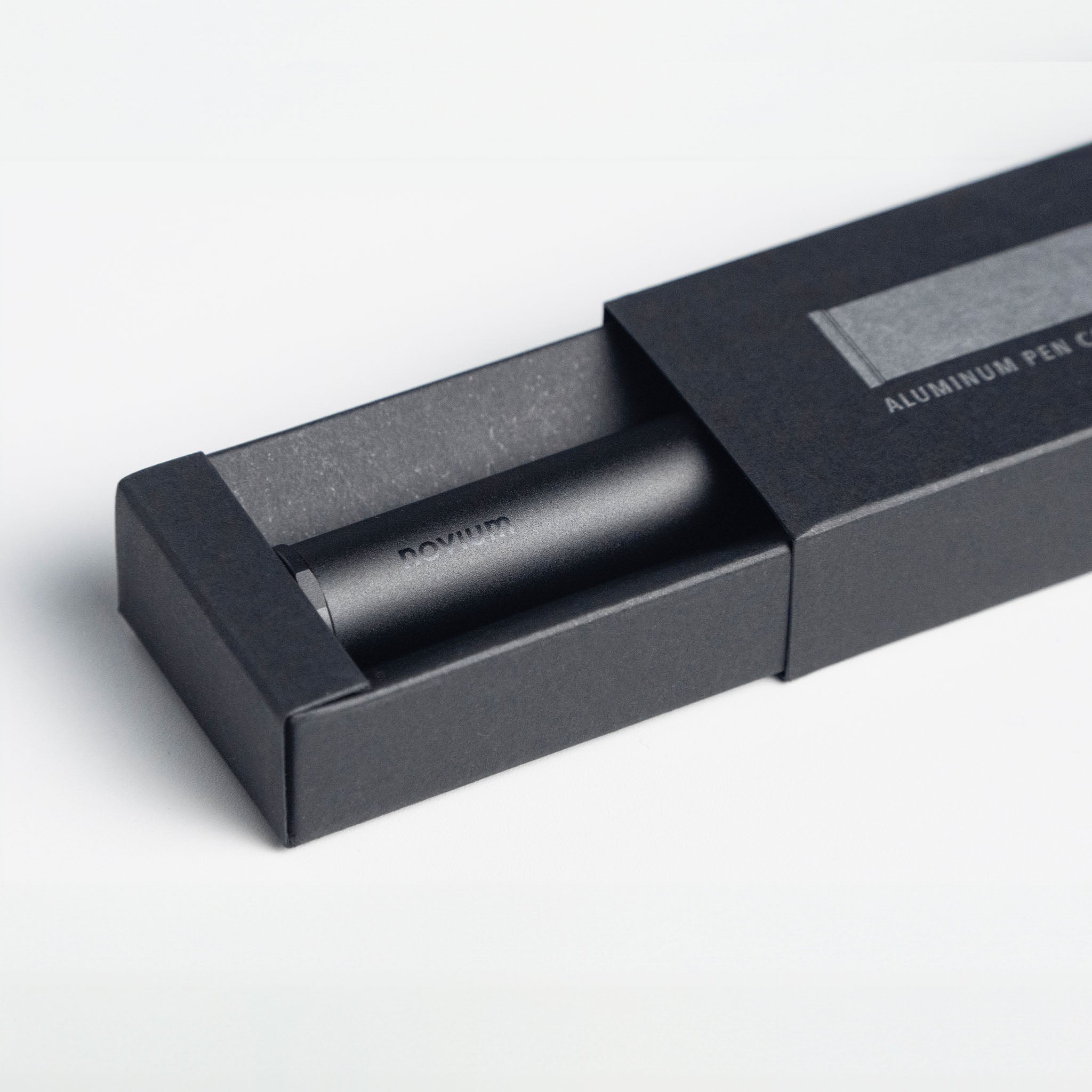 An aluminum pen case with a novium logo on it, a black tube shape, accompanied by its rectangular black box packaging.