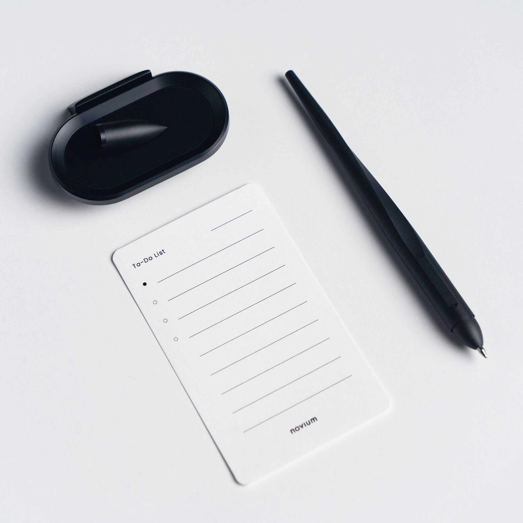 A flat lay of a black hoverpen, a to-do list card with tasks lines, and a card holder on a white surface