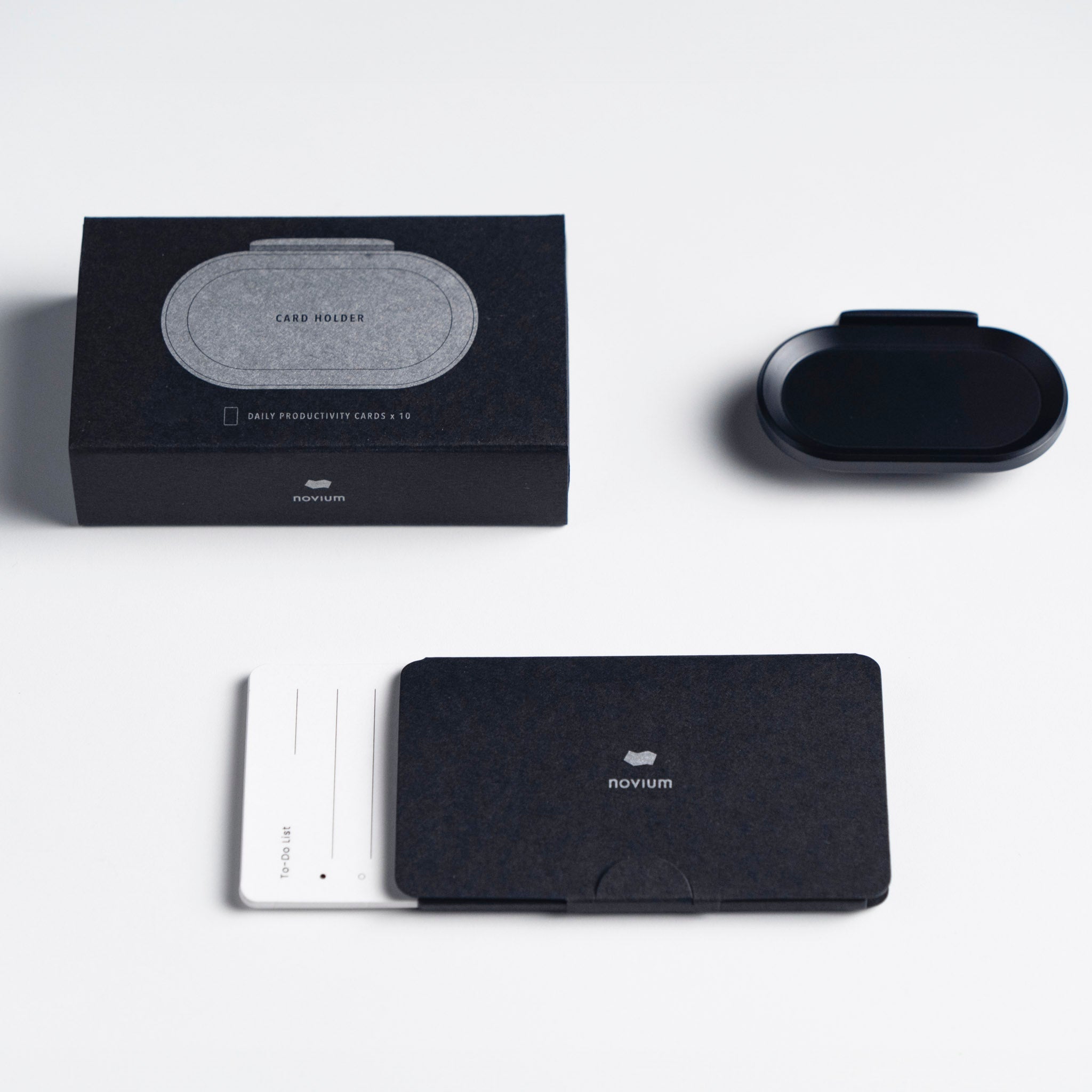 An unboxing of a novium card holder, with a magnetic tray, a packaging black box, and 10 to-do list cards displayed on the desk